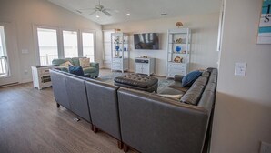 A spacious living room with a grey sectional sofa, a television mounted on the wall, and a ceiling fan. - Experience oceanfront luxury at Ohana Tides, a 5-bedroom retreat in Holden Beach. (Holden Beach)