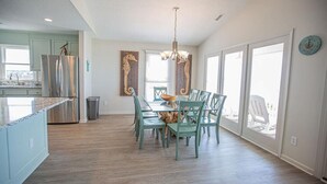 A spacious kitchen with a dining area, large windows, and a view of the outdoors. - Experience oceanfront luxury at Ohana Tides, a 5-bedroom retreat in Holden Beach. (Holden Beach)