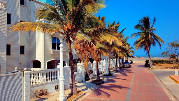 A coastal hotel with a row of palm trees, a red-paved walkway, and a white fence. - Hermosa Casa Playera (Cartagena)