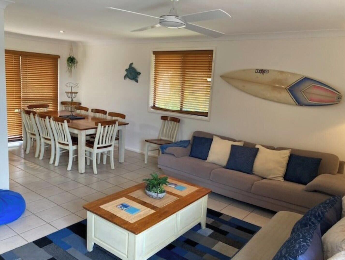 A living room with a sofa, a coffee table, a dining table with chairs, and a ceiling fan.