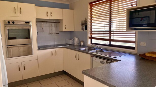 A kitchen with white cabinets, a double oven, a sink, and a window with blinds.