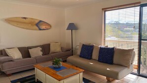 A living room with two sofas, a coffee table, a surfboard, and a lamp.