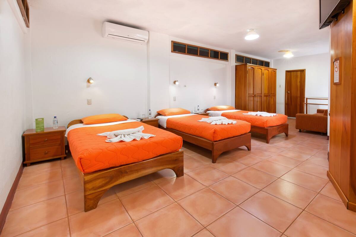 A hotel room with three wooden beds, each with orange bedding, a wooden nightstand, a wooden chair, and a wooden wardrobe.