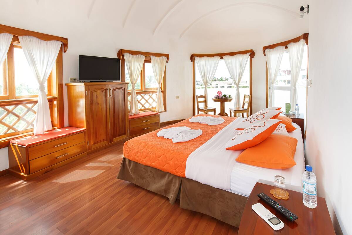 A hotel room with a bed, wooden furniture, a TV, and a small table with a bottle and remote controls.