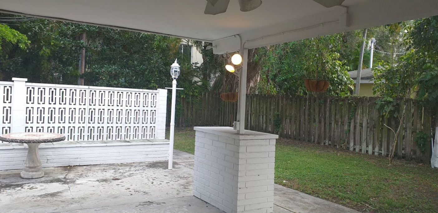 Un patio couvert, agrémenté d’une clôture blanche, d’une petite table et de jardinières suspendues.