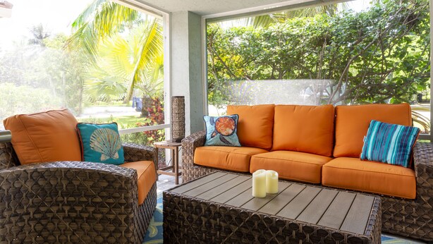 A room with wicker furniture, a wooden coffee table, and a view of lush greenery outside. - Blue Tempo - Steps to Wilton Dr, Heated Salt Pool, Huge Yard (Wilton Manors)