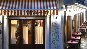 A historic building with a pizza restaurant on the ground floor, featuring a balcony with a person standing, and a row of tables and chairs outside. - Veniceluxury (Venice)