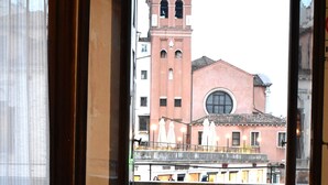 A balcony with a potted plant and a chair, overlooking a building with a bell tower. - Veniceluxury (Venice)