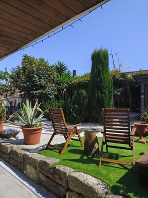 An outdoor patio area with two wooden chairs, a round glass table, and various potted plants.