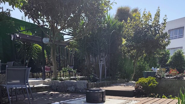 A wooden deck with a lantern, outdoor seating, and a garden area with various plants and a small water feature. - Ruby Charm Houses 8 66132/AL (Porto)