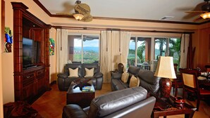 A spacious living room with a large flat-screen TV, leather sofas, a coffee table, and a dining area with a table and chairs. - Luxury Ground Floor  Condo, close to pool access to beach club at Los Suenos. (PUNTARENAS)