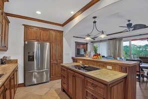 A kitchen with wooden cabinets, a stainless steel refrigerator, a central island with a sink, and a ceiling fan. - Luxury Ground Floor Condo, close to pool access to beach club at Los Suenos. (PUNTARENAS)