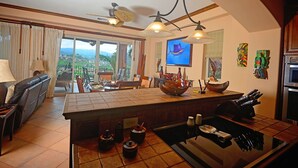 A spacious living area with a large island, a dining table, and a sofa. There is a view of the outdoors through large windows. - Luxury Ground Floor  Condo, close to pool access to beach club at Los Suenos. (PUNTARENAS)