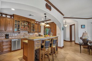 A spacious kitchen with wooden cabinets, a central island with bar stools, and pendant lighting. - Luxury Ground Floor Condo, close to pool access to beach club at Los Suenos. (PUNTARENAS)