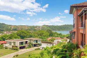A residential area with modern houses, a road, and a view of a lake and hills. - Luxury Ground Floor Condo, close to pool access to beach club at Los Suenos. (PUNTARENAS)