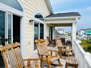 A wooden deck with chairs and a table, a covered area with a railing, and a view of houses in the background.