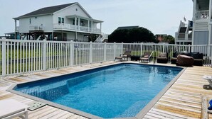 Piscina retangular com deck de madeira, rodeada por uma cerca branca.
