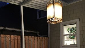 An outdoor patio with a white sofa, a wicker chair, and a hanging light fixture.