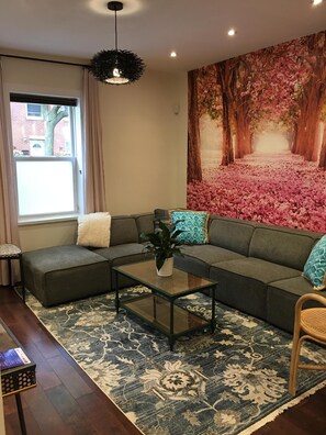 A modern living room with a sectional sofa, a glass coffee table, and a large floral mural on the wall.