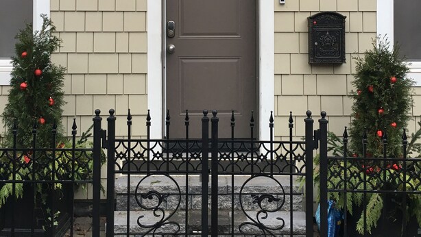A house with a brown door, a number 13 on the wall, and two Christmas trees with red ornaments.