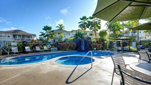 A swimming pool with lounge chairs, a waterfall feature, and palm trees.