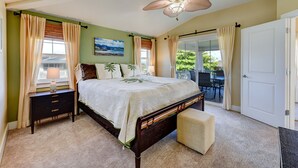 A bedroom with a bed, nightstands, a bench, a ceiling fan, and a view of the outdoors.