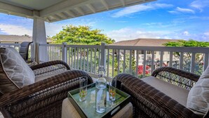 A covered outdoor seating area with wicker furniture and a glass table, overlooking a residential neighborhood.