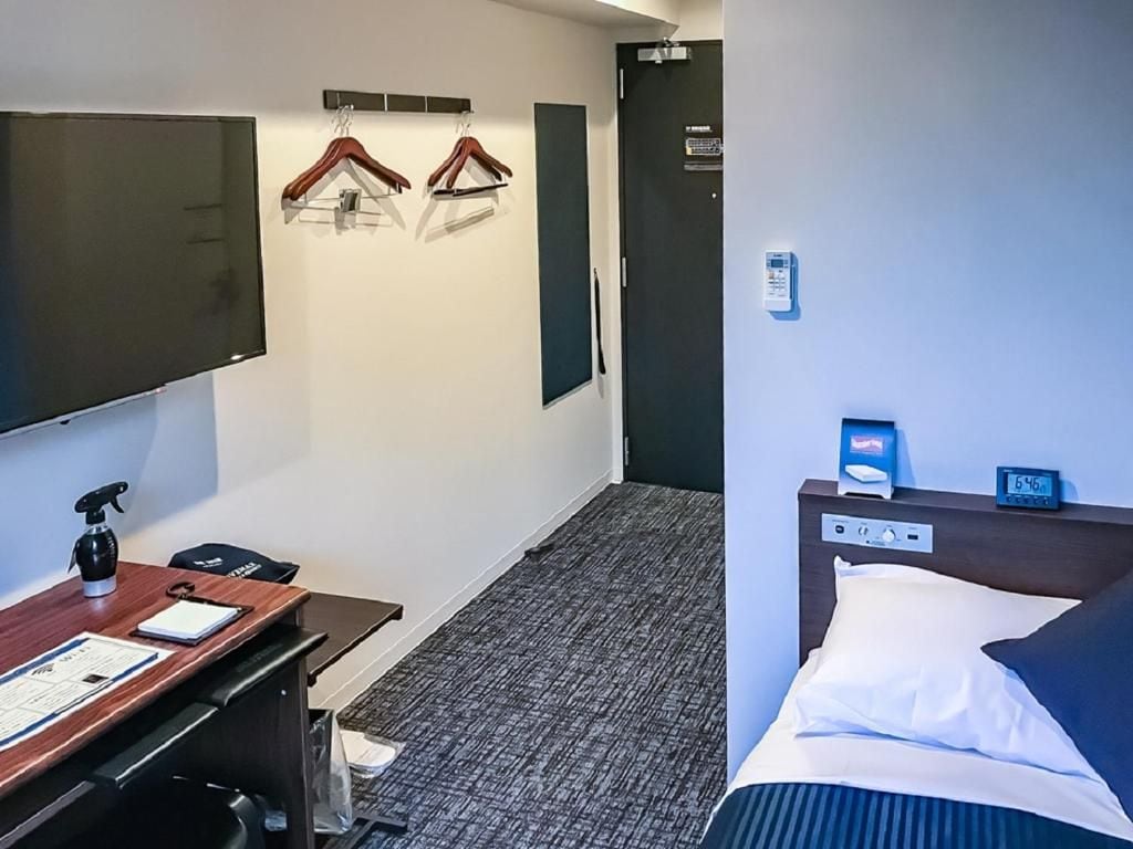 A hotel room with a bed, a desk with a computer, a TV, and a coat rack with hangers.