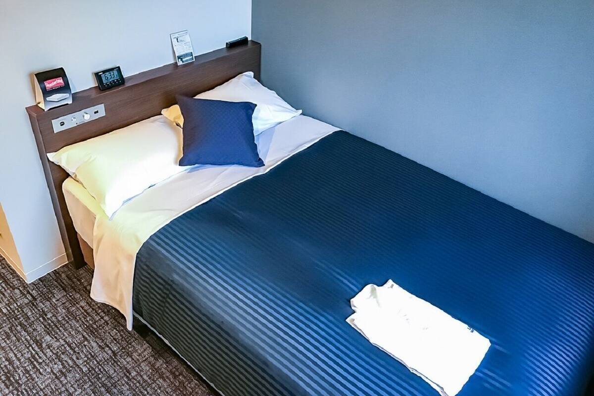 Een hotelkamer met een bed, nachtkastje, klok en afstandsbediening.
