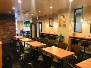 L’intérieur d’un restaurant présente de nombreuses tables et chaises en bois, un mur décoratif en briques et des luminaires suspendus.