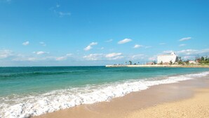 A beach with clear blue water, a sandy shore, and a building in the background. - Irie House (Onna)