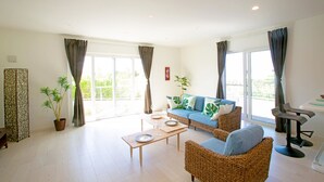 A spacious living room with a sofa, chairs, a coffee table, and a potted plant. - Irie House (Onna)