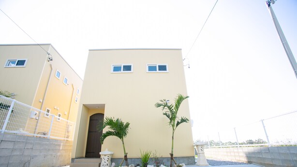 A building with a beige facade, a gated entrance, and two palm trees in the foreground. - Irie House (Onna)