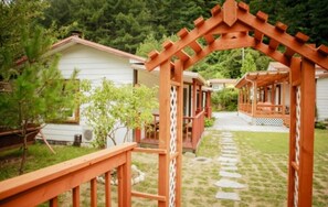A wooden pergola structure in a garden area with a pathway leading to a white building.
