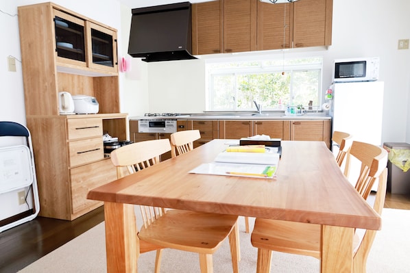 A modern kitchen with wooden cabinets, a dining table with chairs, a microwave, and a window providing natural light.