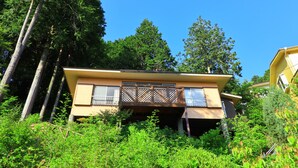 A two-story house with a balcony, surrounded by dense greenery and tall trees. - Angel Forest Fuji Komatsugahara (Izunokuni)