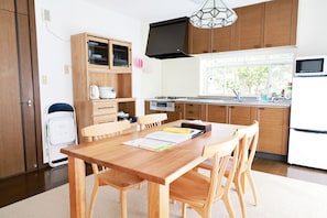 A modern kitchen with wooden cabinets, a dining table with chairs, a built-in oven, and a window with a view of trees.