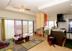 A spacious living area with a dining table, chairs, a kitchen area, and a ceiling fan. - Araha Ryukyu Style (Chatan)