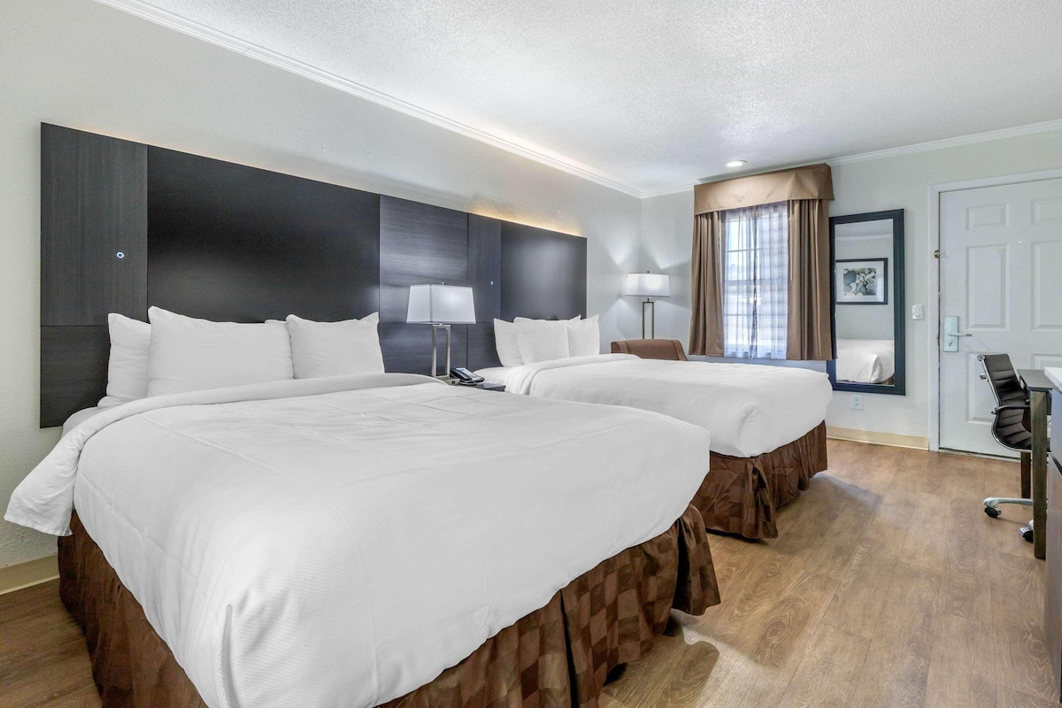 A hotel room with two beds, a desk, and a chair.