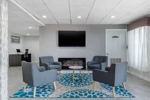 A modern lounge area with two armchairs, a small round table, and a flat-screen TV mounted on the wall. - Suburban Studios at the University (Conway)