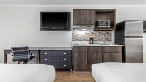 Een kleine hotelkamer met een bed, bureau, stoel, flatscreen-tv, magnetron, koffiezetapparaat en koelkast.
