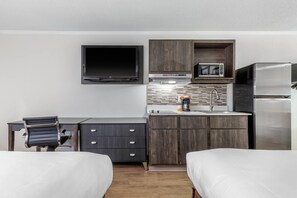 A compact hotel room with a bed, a desk, a chair, a flat-screen TV, a microwave, a coffee maker, and a refrigerator. - Suburban Studios at the University (Conway)