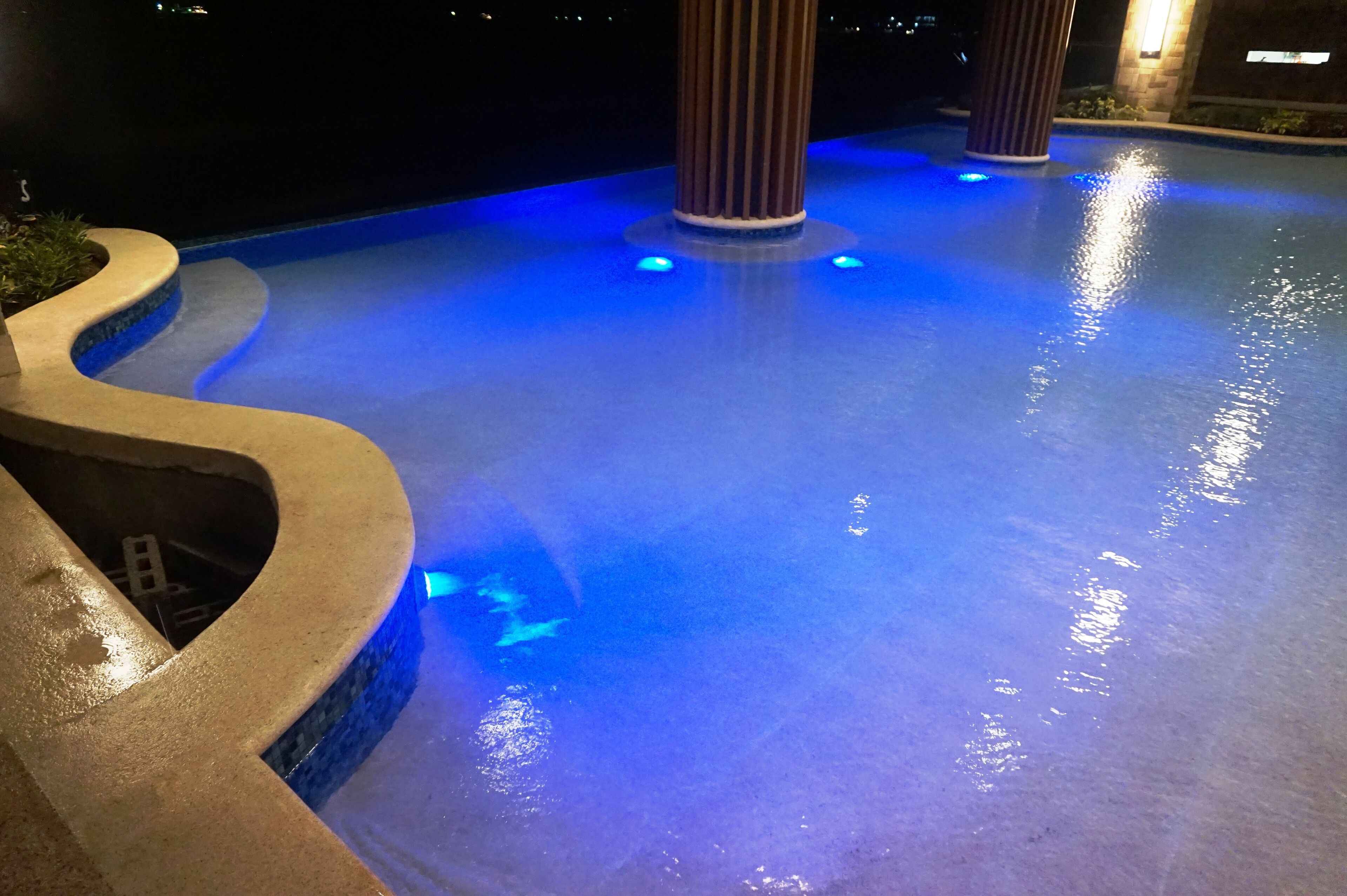 A nighttime pool area with blue lighting and a stone pathway.