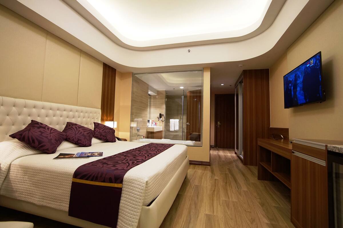 A modern hotel room with a large bed, a television, a bathroom, and a desk.