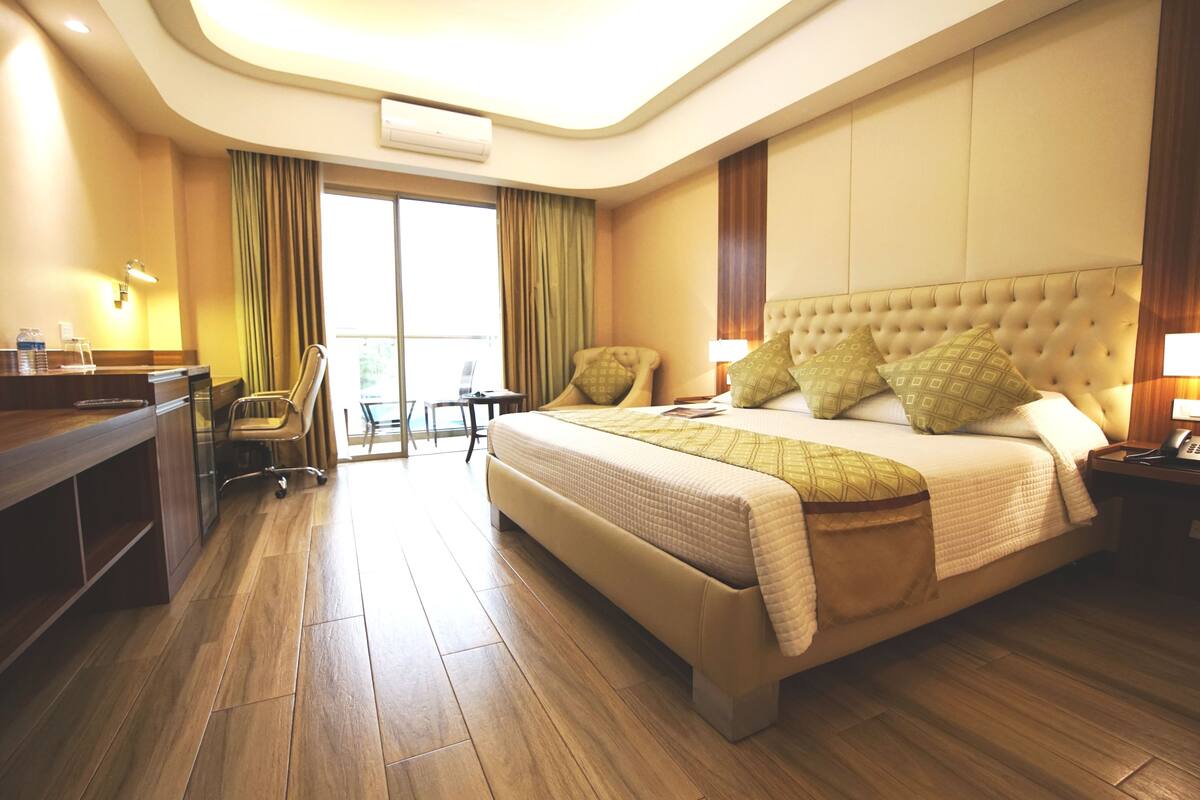 A hotel room with a large bed, a desk, a chair, and a view of the outdoors.