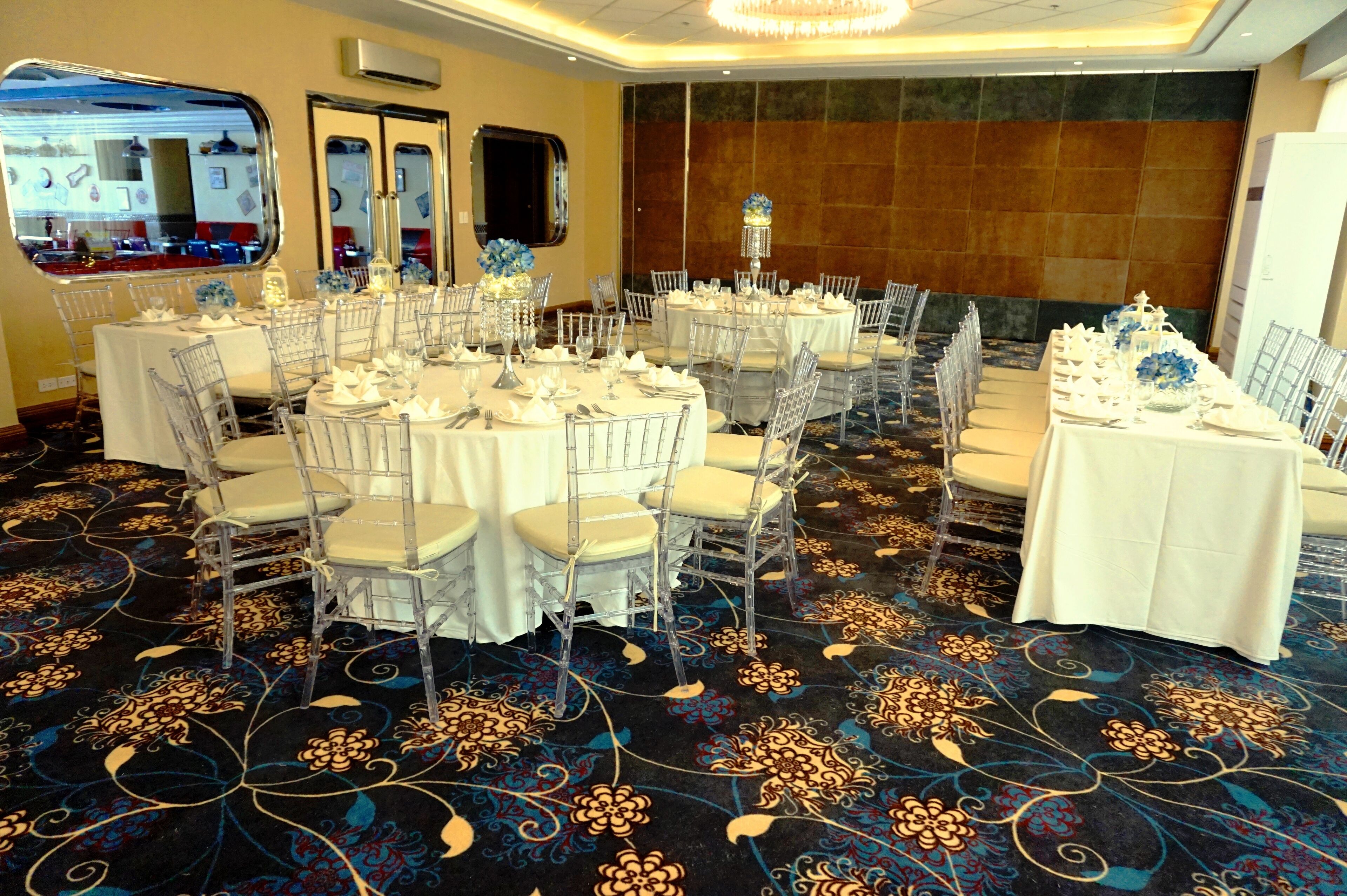 Un salón de banquetes con mesas redondas, sillas transparentes y centros de mesa florales.