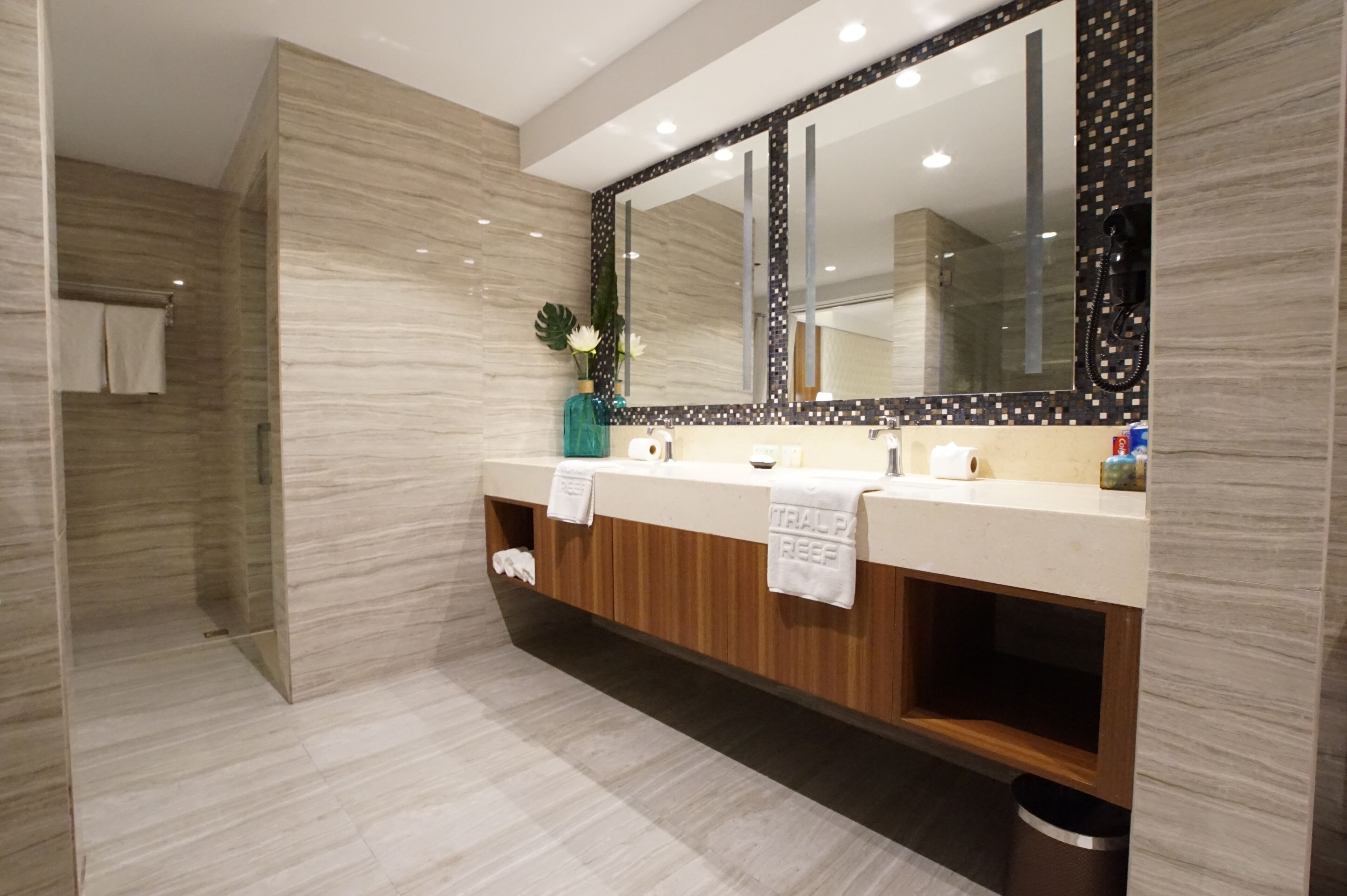 A modern bathroom with a large mirror, wooden vanity, and a glass shower enclosure.