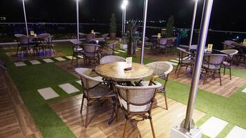 An outdoor patio with round tables and wicker chairs, surrounded by artificial grass and wooden flooring.