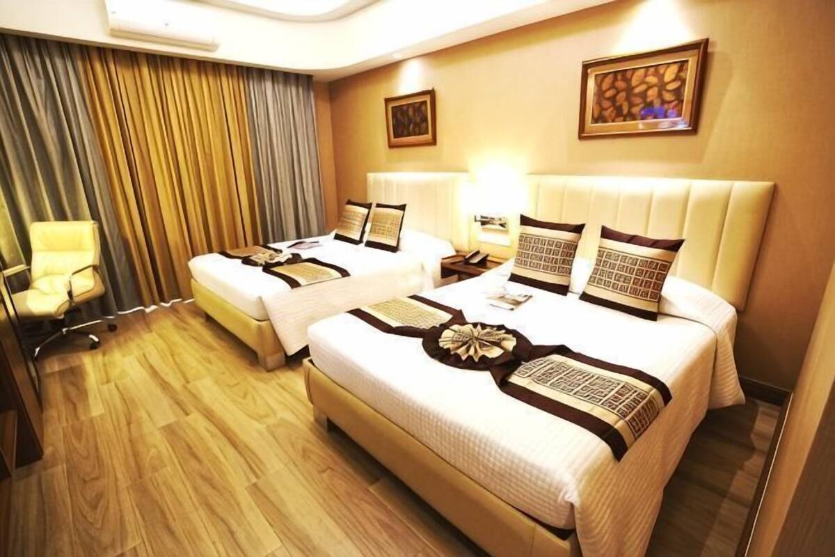A hotel room with two beds, a desk, a chair, a lamp, and a curtain.