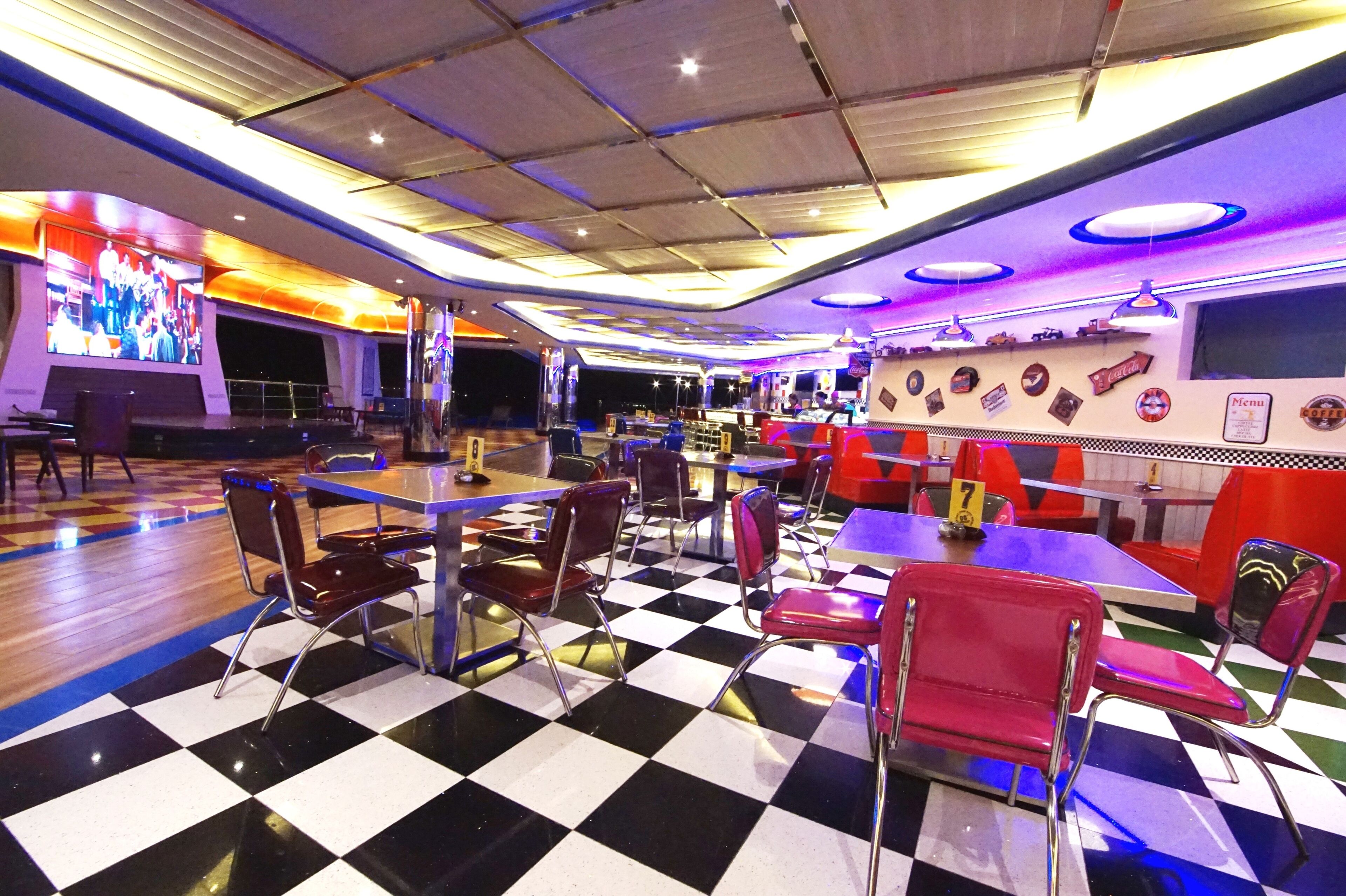 A retro-themed restaurant with checkered flooring, vintage chairs, and neon lighting.